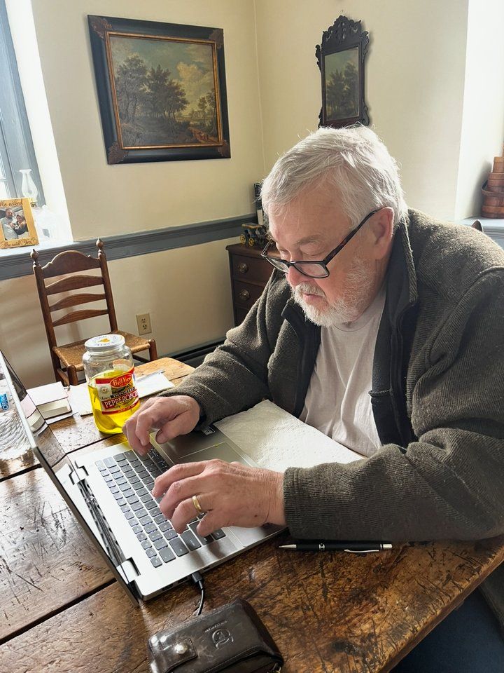 Kevin Damewood writing at a laptop at an old wooden table